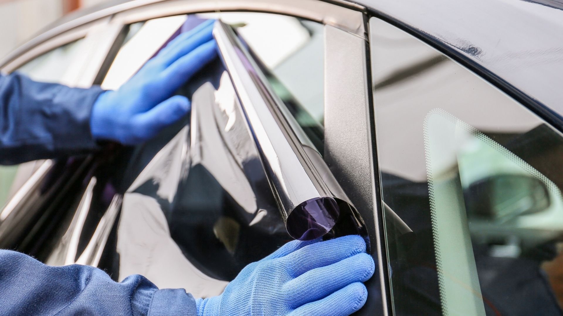 Hands in blue gloves applying tint film to car window