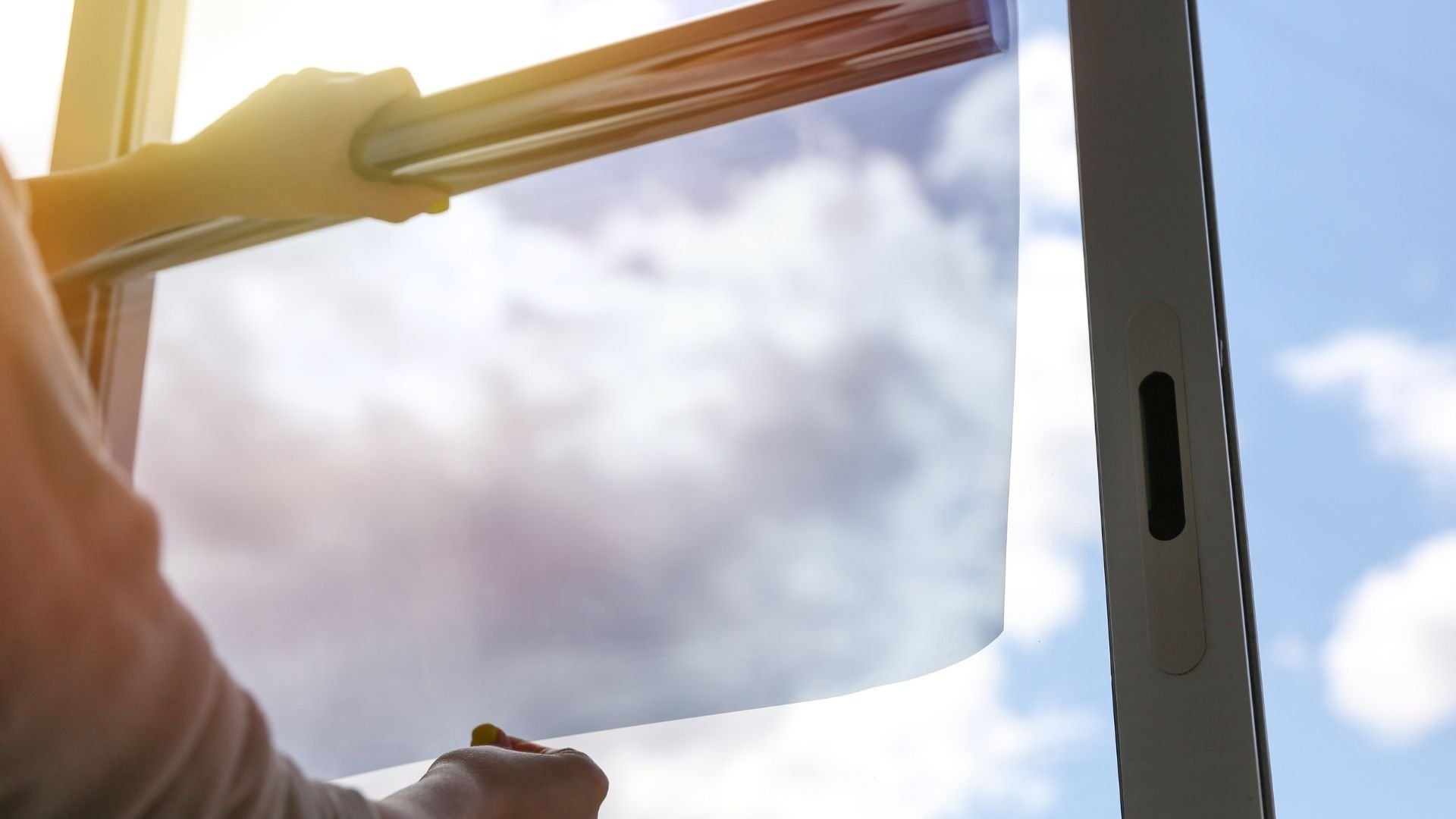 Hand pulling down window blind with sunlight streaming through