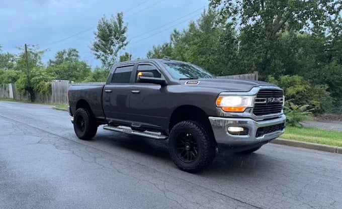 Gray RAM 2500 pickup truck parked on wet road with trees in background