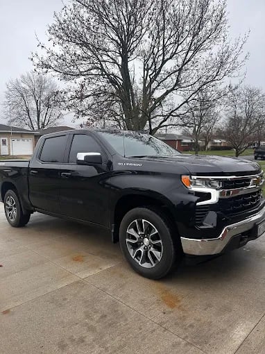 Black Chevrolet Silverado pickup truck parked on concrete driveway near trees